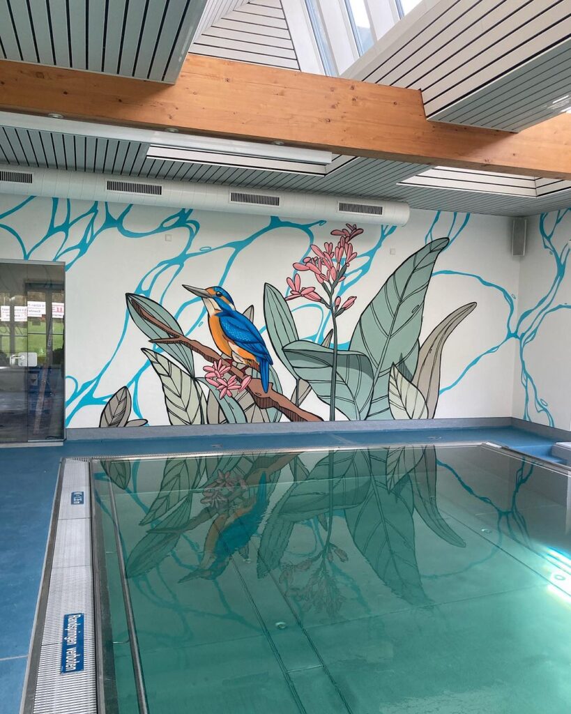 Wandgemälde eines Vogels und tropischer Pflanzen an einer Poolwand, reflektiert im Wasser.