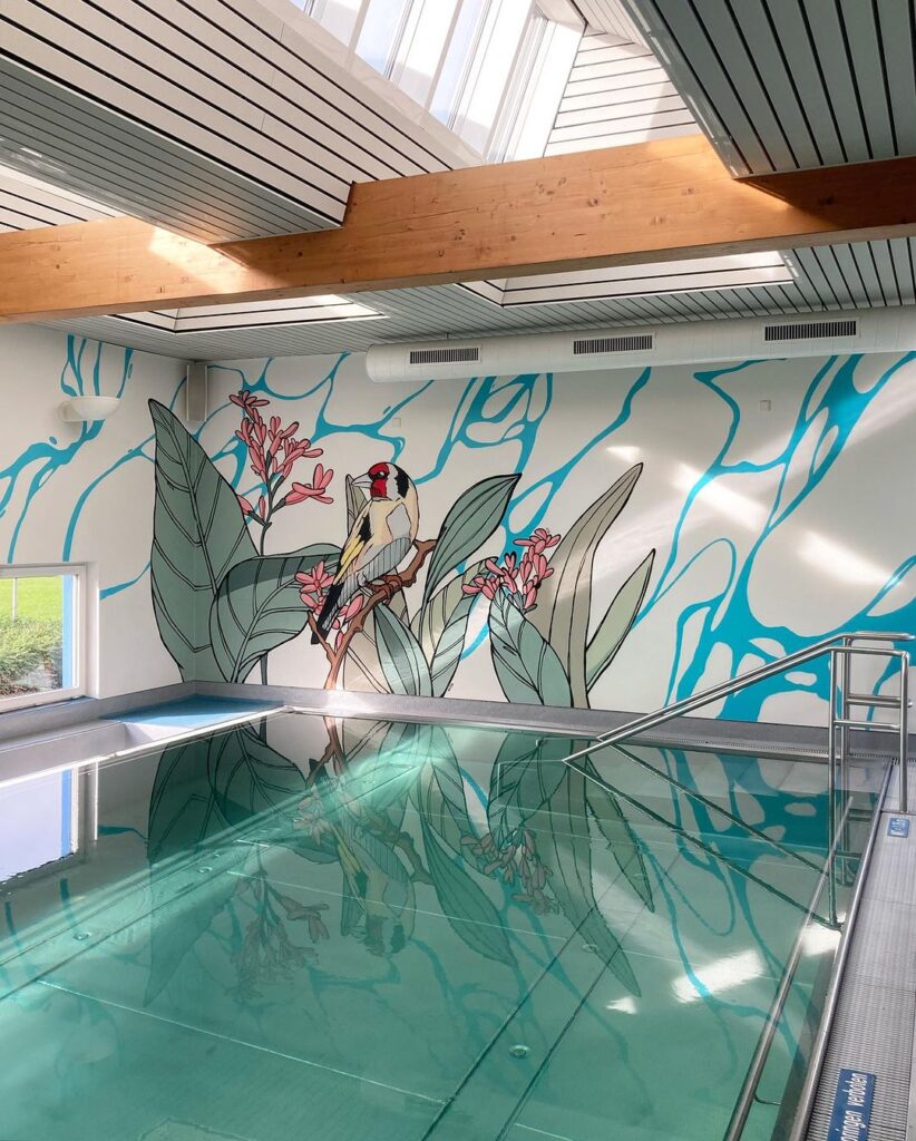 Wandgemälde eines Vogels und tropischer Pflanzen an einer Poolwand, reflektiert im Wasser.
